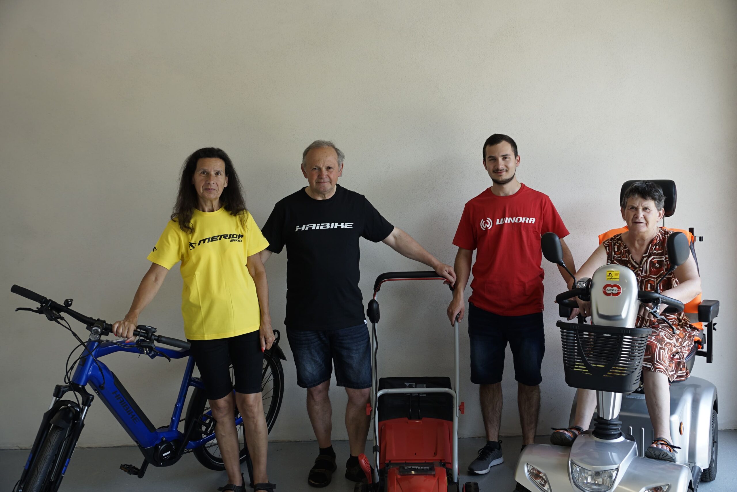 Ein Familienfoto der Familie Weinhandl. Christa, Helmut und Johannes Weinhandl neben einem E-Bike und einem Rasenmäher. Anita sitzt auf einem Seniorenmobil.