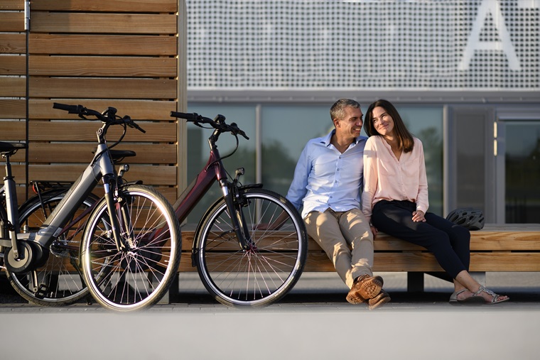 2 Personen neben abgestellten Fahrrädern auf einer Holzbank.